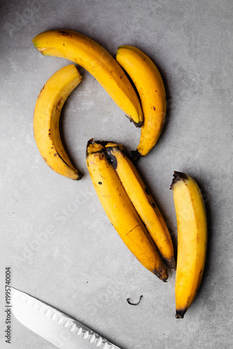 Overhead view of ripe plantains on grey countertop, top view of overripe yellow plantains on grey background, ripe plantains being prepared for frying