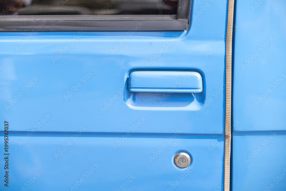 Obraz premium Close up detail of bright blue truck door handle and lock cylinder showing smooth painted metal surface conveying calm and steady mood perfect for transportation themes