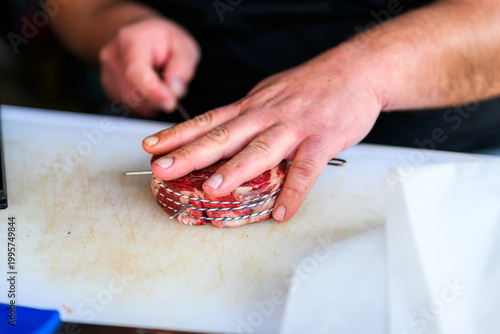 Close-up of a chef in black nitrile gloves precisely trimming a thick-cut ribeye steak with a sharp knife on a cutting board during a professional Steak Cookoff Association (SCA) BBQ competition.