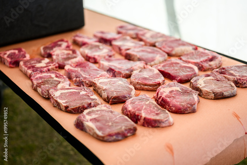 Rows of raw, marbled ribeye steaks laid out on butcher paper during a Steak Cookoff Association (SCA) BBQ competition, showcasing premium meat quality and preparation for professional grilling.