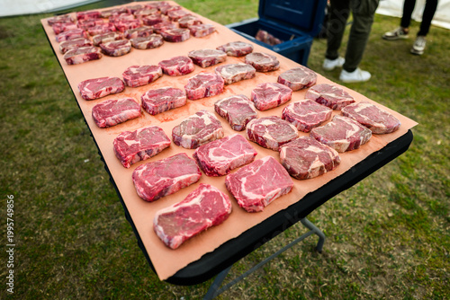 Rows of raw, marbled ribeye steaks laid out on butcher paper during a Steak Cookoff Association (SCA) BBQ competition, showcasing premium meat quality and preparation for professional grilling.