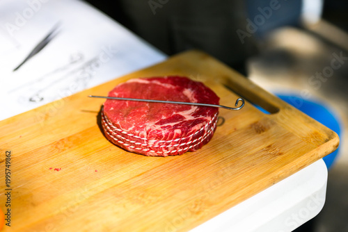 A perfectly trimmed and trussed raw ribeye steak sits on a wooden cutting board with a metal skewer, prepared for high-stakes professional grilling at a Steak Cookoff Association (SCA) BBQ competition