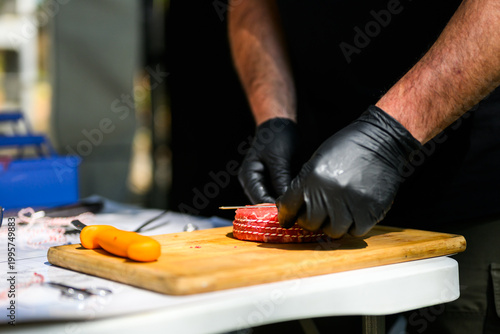 Close-up of a chef in black nitrile gloves precisely trimming a thick-cut ribeye steak with a sharp knife on a cutting board during a professional Steak Cookoff Association (SCA) BBQ competition.