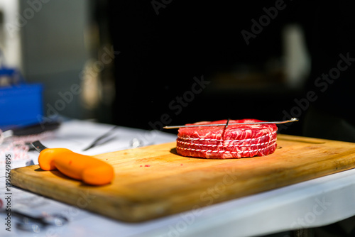 A perfectly trimmed and trussed raw ribeye steak sits on a wooden cutting board with a metal skewer, prepared for high-stakes professional grilling at a Steak Cookoff Association (SCA) BBQ competition