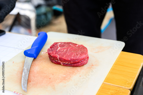A perfectly trimmed and trussed raw ribeye steak sits on a wooden cutting board with a metal skewer, prepared for high-stakes professional grilling at a Steak Cookoff Association (SCA) BBQ competition