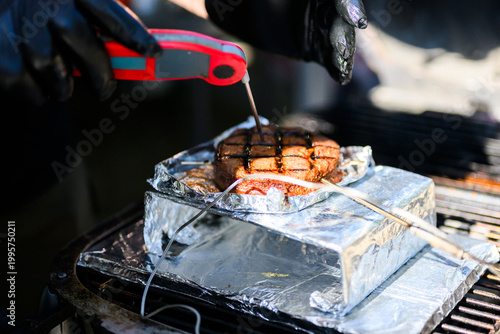 A close-up action shot of a chef using a digital instant-read thermometer to check the internal temperature of a perfectly seared ribeye steak during a professional SCA BBQ competition.