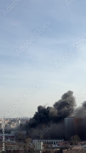 Thick black smoke rising over city from large fire, environmental pollution and urban disaster concept