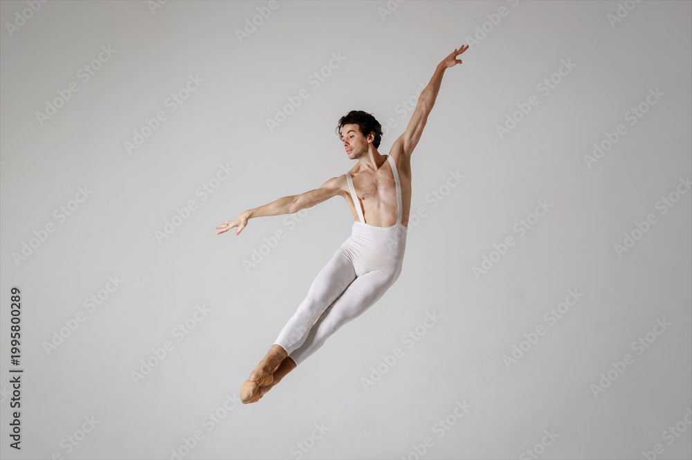 Fototapeta premium Graceful male ballet dancer in mid-air leap on grey background, classical ballet pose