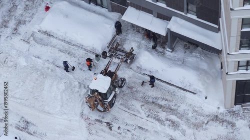 Snow removal in residential yard with tractor and workers, clearing area after snowfall, winter urban maintenance
