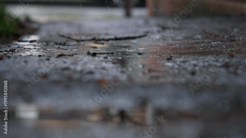 Close-up of wet asphalt surface during rain. Raindrops create small splashes and water movement on the ground. Shallow depth of field, urban outdoor scene, weather and environment concept