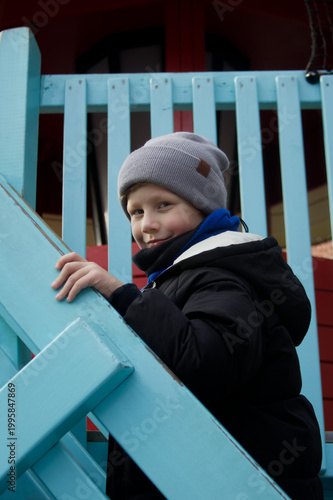 Smiling blond boy climbing blue wooden stairs on a playground