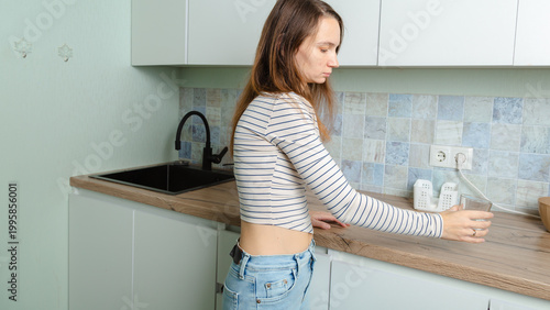 happy woman holds a glass of clean water in a modern kitchen. Hydration, healthy lifestyle, and daily wellness habits.