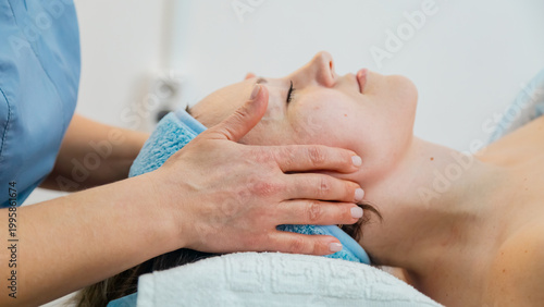 Face massage. Beautiful woman with closed eyes relaxes in spa center during facial massage. Masseuse massages face of client of beauty salon. Concept of skin care, facial massage.