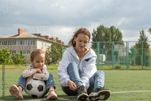 Woman sitting on grass with her daughter at sport field