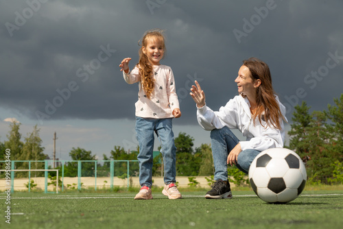 Woman teaching her daughter soccer ball at sport field