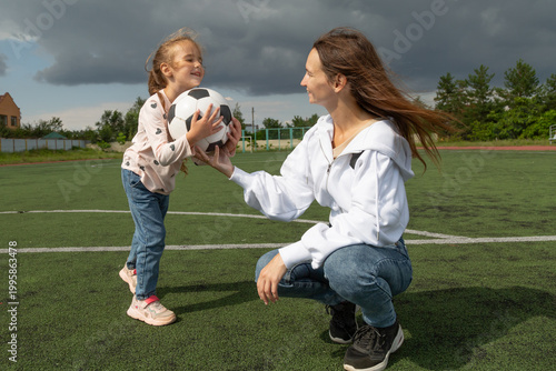 Woman teaching her daughter soccer ball at sport field