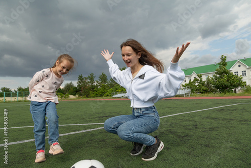 Woman teaching her daughter soccer ball at sport field
