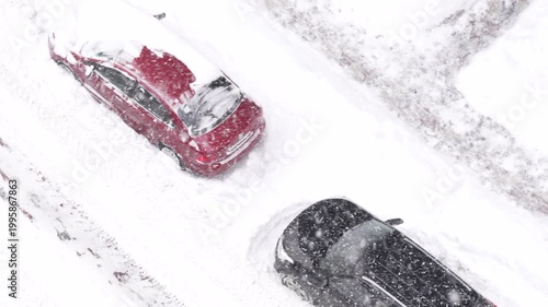 Cars covered with snow during snowfall on urban road, winter weather and transport concept