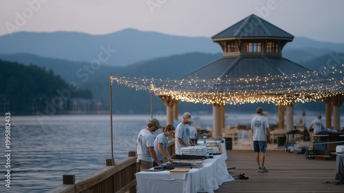 Outdoor Father's Day volunteer fishing tournament setup crew strings lights over lakeside pavilion, early morning mist on water, folding tables, tackle boxes, volunteers in matching shirts, June cha