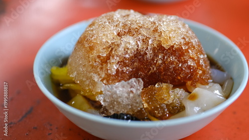 Thai - Chinese shaved ice dessert called Bok Kia, topped with longan syrup red daed, and chewy rice noodles in bowl.