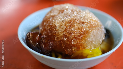 Thai - Chinese shaved ice dessert called Bok Kia, topped with longan syrup red daed, and chewy rice noodles in bowl.