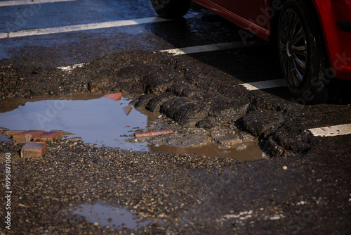 Urban scene with car passing by a big pothole in the asphalt