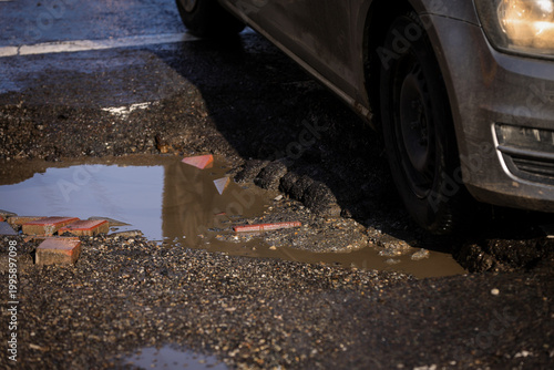 Urban scene with car passing by a big pothole in the asphalt