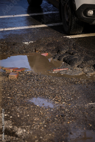 Urban scene with car passing by a big pothole in the asphalt
