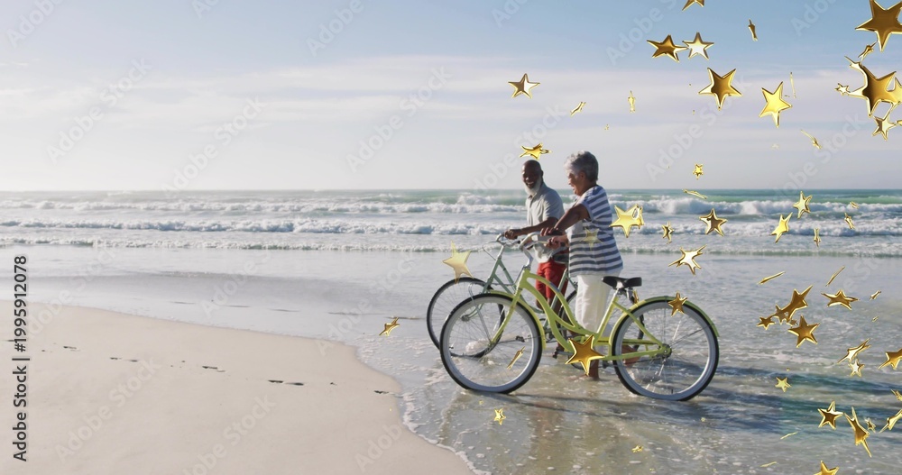 Fototapeta premium Walking couple wearing striped top holding cruiser bikes at surf with gold stars, copy space