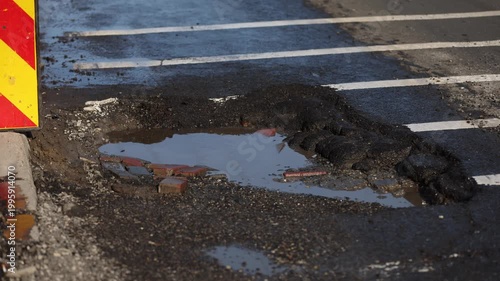 Urban scene with car passing by a big pothole in the asphalt