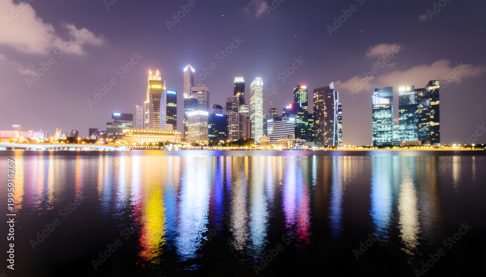 Obraz premium Illuminated modern city skyline reflecting on calm harbor at night.