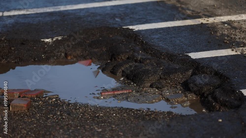 Urban scene with car passing by a big pothole in the asphalt