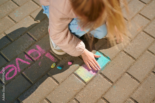 Child drawing with colorful chalk on outdoor pavement.