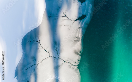 Aerial view of frozen lake with ice patterns and turquoise water, winter landscape, destination concept. Fusine lakes, Tarvisio, Friuli, Italy.
