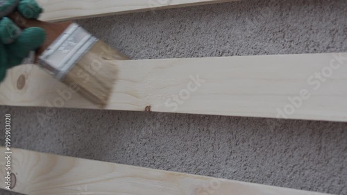 Close-up of a gloved hand painting a wooden board with a brush, applying white paint. Home improvement, DIY renovation, wood treatment and surface coating concept with copy space.