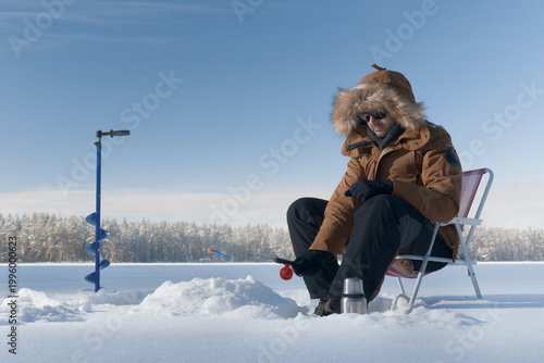 Man ice fishing alone on a frozen lake, enjoying solitude, calm and escape from urban life.