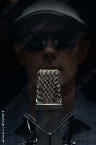 Close up of professional studio microphone with blurred male host in background. Concept of podcast recording, voice, broadcasting and audio content creation.