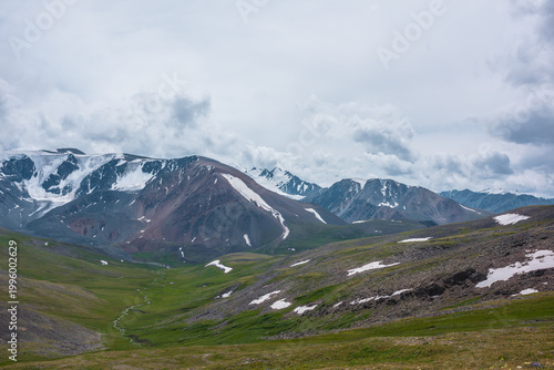 Dramatic view to green alpine valley with long creek and large snow-capped mo...