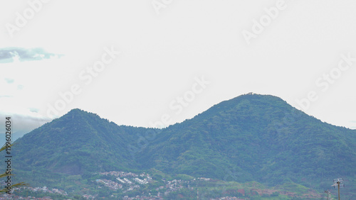 A serene rural landscape featuring a lush green mountain under a bright sky, with farmland in the foreground and scattered trees across the countryside.