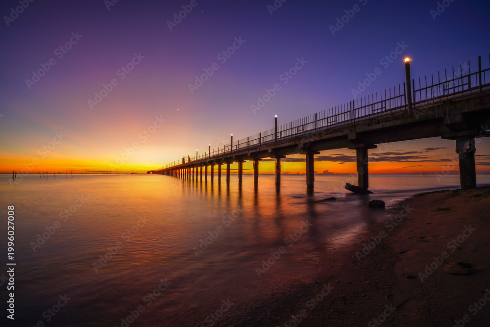 Fototapeta premium Long pier stretching into the sea during a golden sunset.