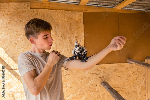 A young man looks at his pet pigeon sitting on his arm