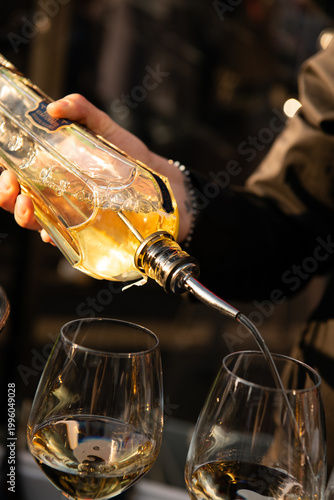 Close-up of elegant white wine being poured into glasses from a decorative bottle, warm ambient lighting creating a refined, intimate bar or restaurant atmosphere.