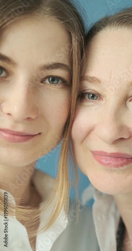 Beautiful mature mother and adult daughter with blue eyes looking at camera close up in the photostudio on blue paper background. Two female generations. Mother's day concept