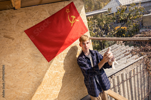 A young man holds a white pigeon, standing by a USSR flag