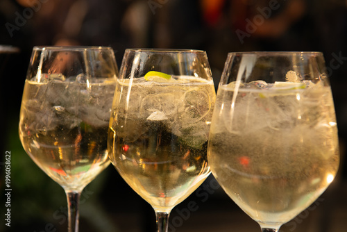 Three elegant glasses of sparkling white wine with ice and lime, glowing in warm ambient light, capturing a festive, upscale bar atmosphere.