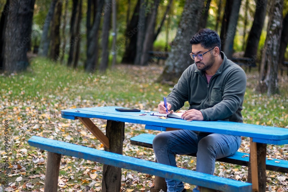Fototapeta premium A Latino man writes under the trees in the landscape