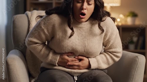 Young woman in pain clutching her stomach while sitting at home