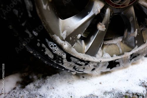 Foto Cleaning car wheel with soap and water in a backyard during a sunny afternoon The suds are visible on the shiny rim