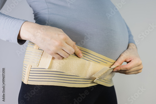 Canvas Print Pregnant woman adjusting a supportive maternity belt over her grey shirt to alleviate back pain and provide abdominal stability during pregnancy