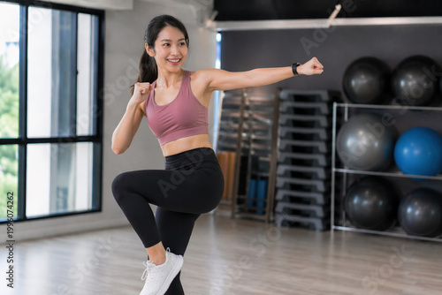 Smiling young Asian woman practicing boxing punch move during fitness class in modern gym